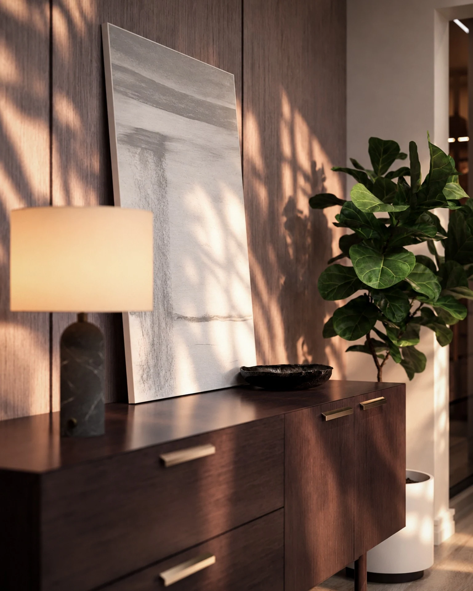 Detalhe da marcenaria em madeira escura da Suíte Refúgio, com luminária de mesa, quadro decorativo apoiado, planta ornamental e luz solar sobre o painel.